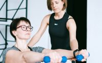 A personal trainer guides a woman lifting dumbbells in an indoor fitness session.